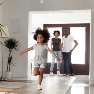 a young girl running down the hallway of her home as her parents watch from the doorway with smiles on their face