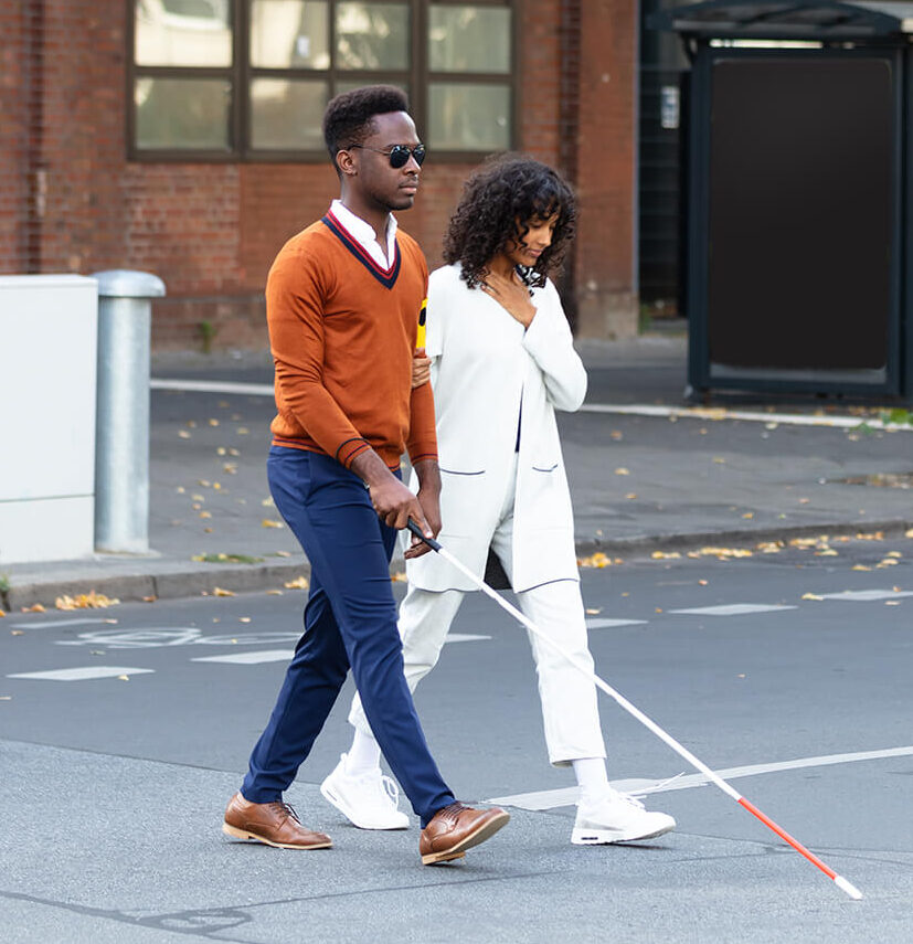 a woman holding a man with a white cane by the arm as she accompanies him across the street