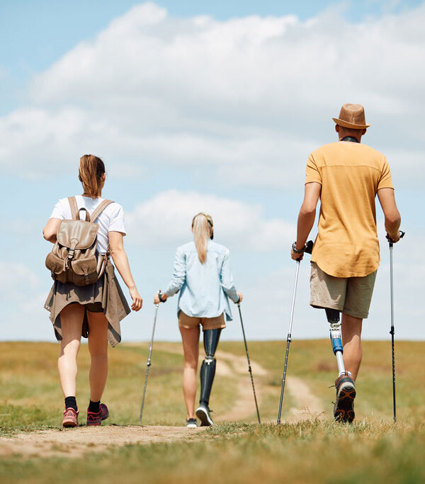 Hikers with prosthetic legs and walking sticks walking together through an open field