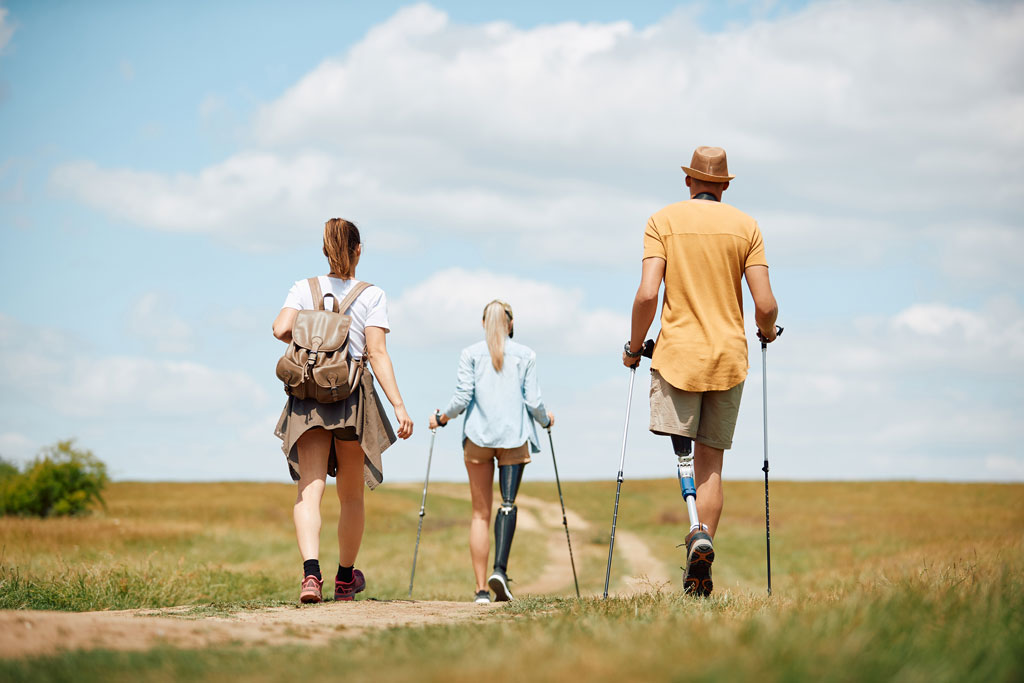 an image of hikers with prosthetic legs and walking sticks walking together through an open field on a clear day